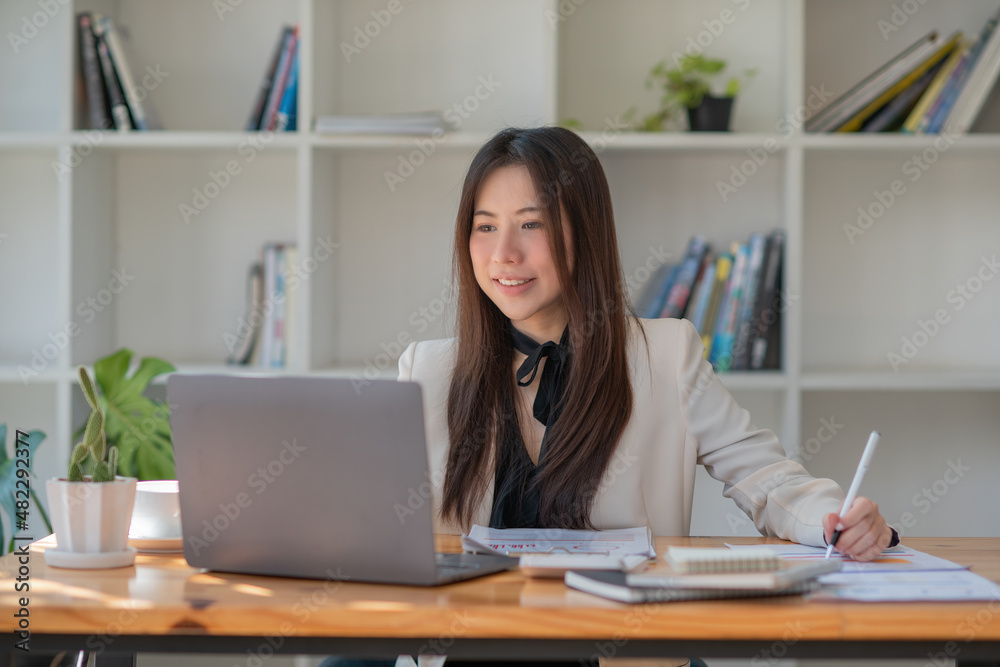 Smiling young Asian businesswoman using a computer at home office workplace Smiling young Asian businesswoman using a computer at home office workplace
