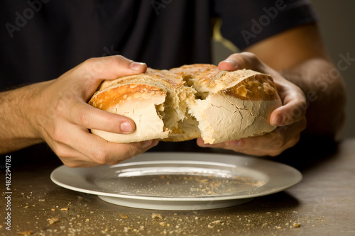 Homem de camisa preta repartindo o pão com o prato em baixo. (ID: 482294782)