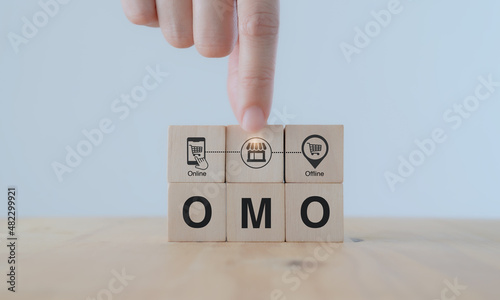 Online merge offline (OMO) concept. Borderless marketing channel conbination strategy creating new opportunities, sales increasing. Hand puts wooden cubes with combination of online and offline icon.