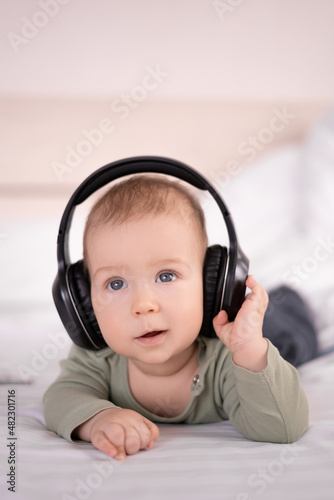 charming baby lying on a white background in headphones listens to music. infant 3 month old with headphones young DJ