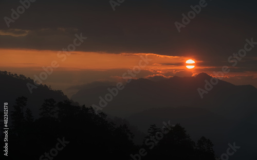 A part of Sun  that behind dark cloud  is going down over mountain ridge and mountain range in an evening