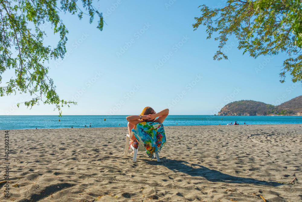 Obraz premium Girl relaxed on a chair looking at the horizon on a beach, on a sunny day.