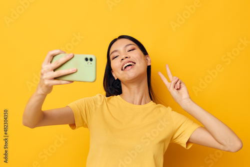 Charming young Asian woman in a yellow t-shirt looking at the phone posing Lifestyle unaltered