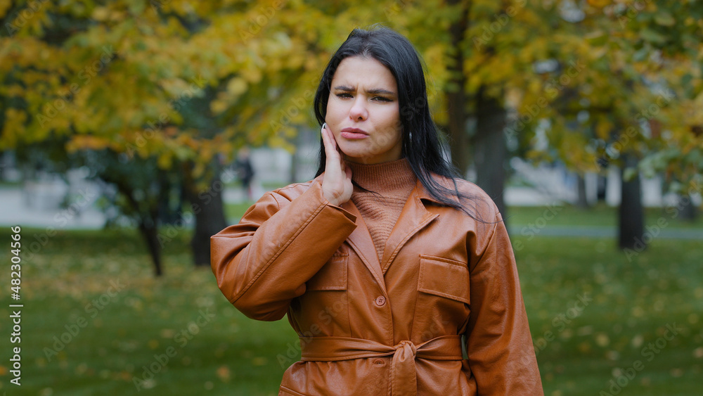 Young hispanic woman standing outdoors feeling toothache holding hand on cheek jaw has dental problems suffering from pain unpleasant symptoms needs treatment tooth decay oral cavity caries problem