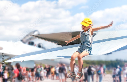 A little girl is sitting on the wing of the plane with her arms outstretched and dreaming of flying  photo