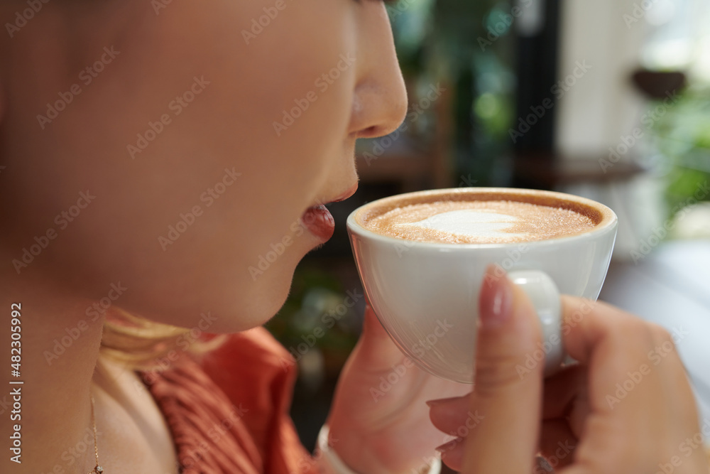 Closeup image of young woman drinking cup of delicious cappuccino Closeup image of young woman drinking cup of delicious cappuccino
