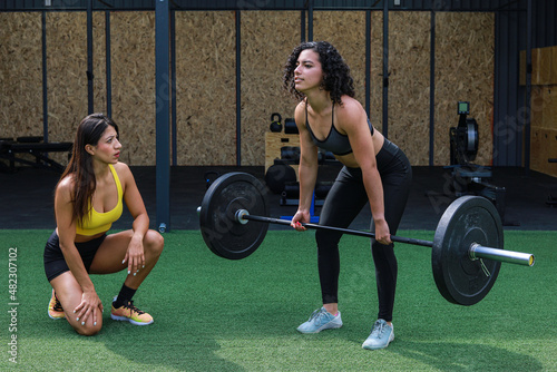 Trainer teaching woman to lift weights inside a crossfit GYM