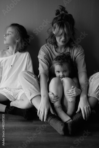 Mother and two funny daughters laughing and playing together. Sisters. Friendship. Family relationships. Green wall. Love and happiness. Emotional and cute girls . Casual home clothes. Black and white