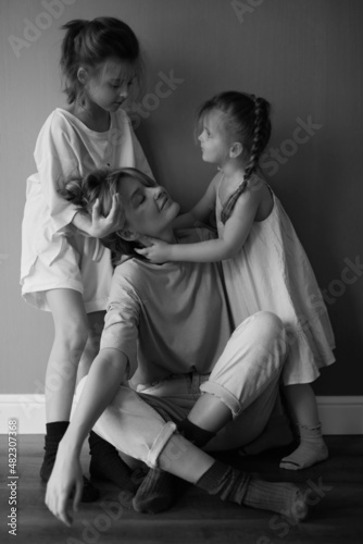 Mother and two funny daughters laughing and playing together. Sisters. Friendship. Family relationships. Green wall. Love and happiness. Emotional and cute girls . Casual home clothes. Black and white