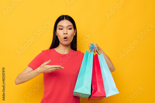 Charming young Asian woman with colorful bags posing shopping fun yellow background unaltered