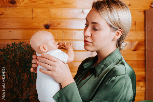 Foto Portrait of pretty caucasian young woman holding newborn baby doll in arms and looking at her while standing indoors