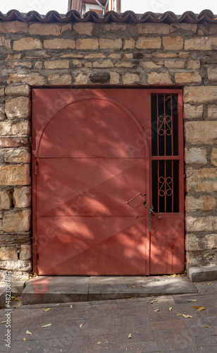 Red metal door with lattice closed on chain with lock in old stone wall. Vertical photo. © Vladimir Kazakov
