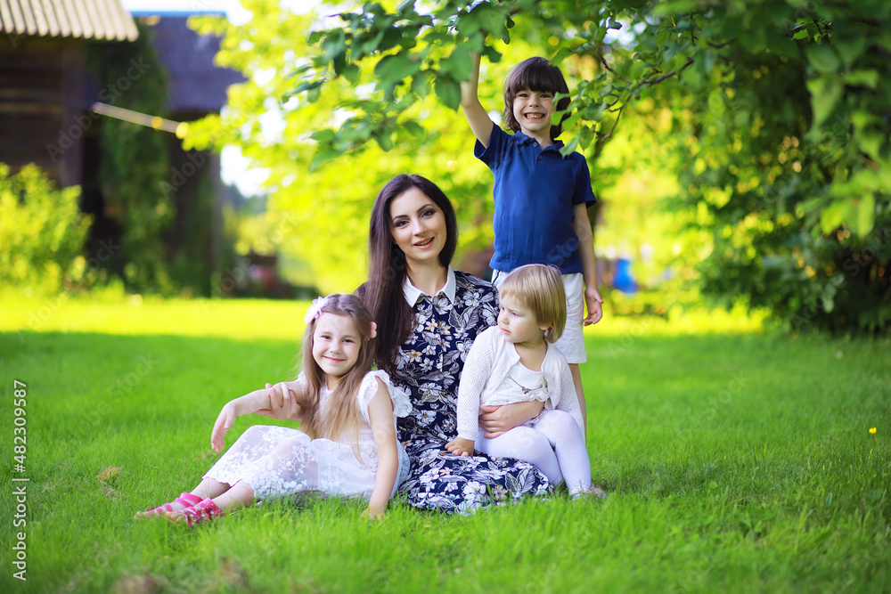 Obraz premium Young large family on a summer morning walk. Beautiful mother with children is playing in the park.