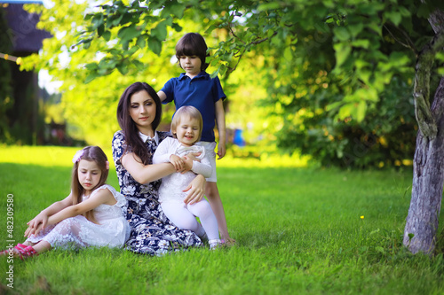 Young large family on a summer morning walk. Beautiful mother with children is playing in the park.