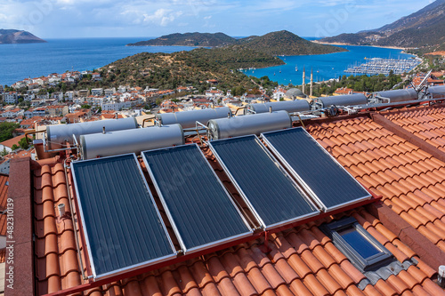 Solar water heater installed on tile roof of house for economical heating of water. A lot of large water tanks. Horizontal photo.