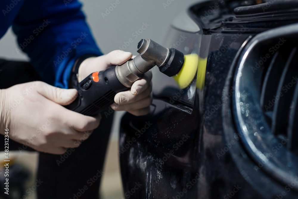 The worker polishes optics of headlights of the car with the electric tool.