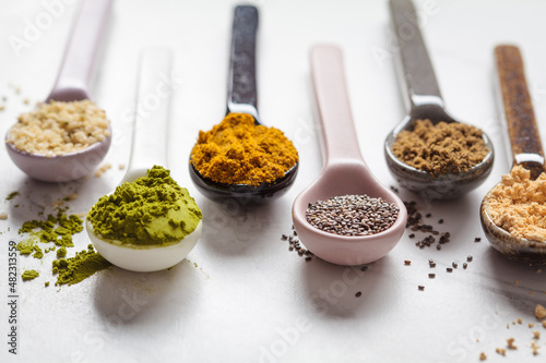 Super food powders in spoons, white marble background.