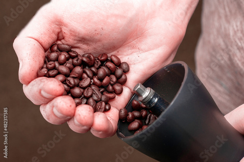 a man grinds coffee in a manual coffee grinder to pour coffee beans into a coffee grinder close-up