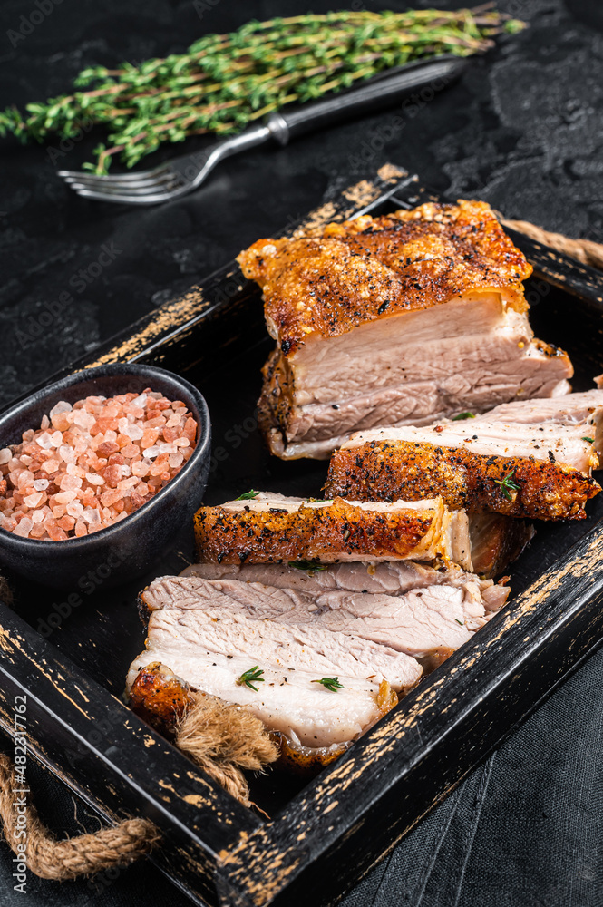 Crispy Roast Pork Belly. Sliced roasted meat with crust in a tray with spices. Black background. Top view
