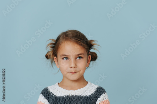 Tight-lipped little girl in striped sweater, hair in buns over blue background. photo