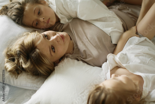 Mother and two funny daughters are laughing and playing together. Sisters. Friendship. Family. Bedroom. Pillows and blanket. Love and happiness. Emotional and cute girls . Casual home clothes. 