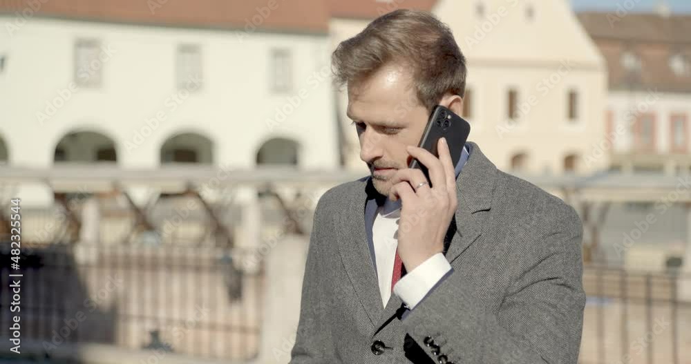attractive businessman in suit being outside, talking to the phone and smiling while standing in front of medieval city background attractive businessman in suit being outside, talking to the phone and smiling while standing in front of medieval city background