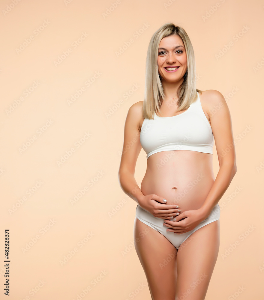 Young pregnent woman in lingerie posing on a beige Young pregnent woman in lingerie posing on a beige