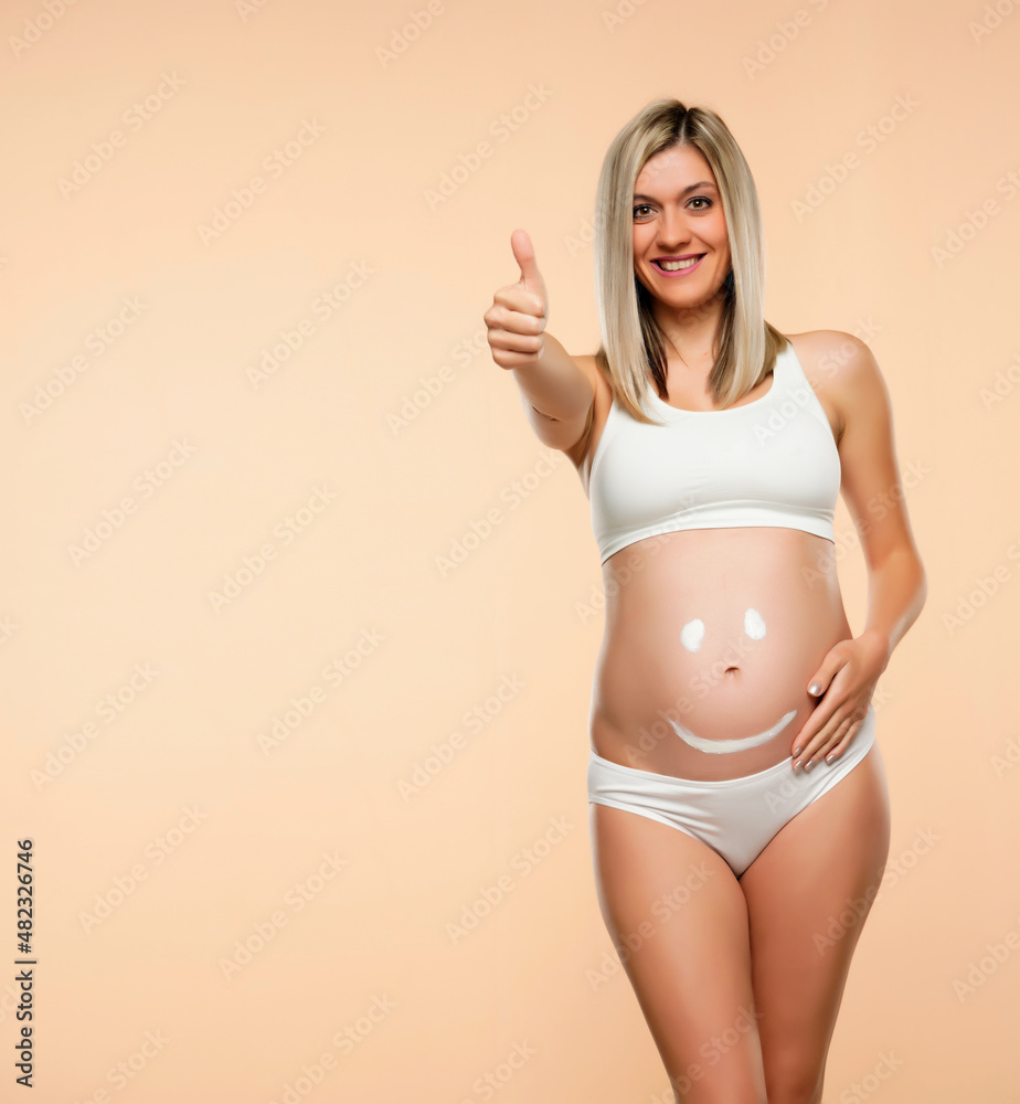 Future mother posing with a smiley face drawing on her belly and showing thumb up Future mother posing with a smiley face drawing on her belly and showing thumb up