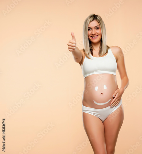 Future mother posing with a smiley face drawing on her belly and showing thumb up