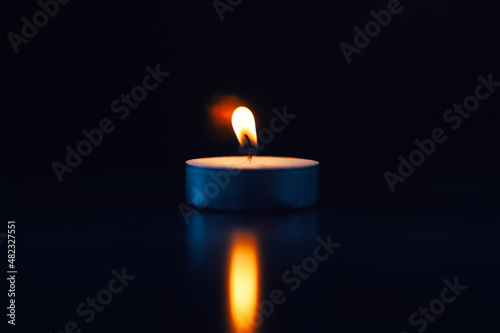 Burning candle with fading flame with reflex, black background
