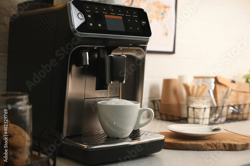 Modern coffee machine making cappuccino in office kitchen, space for text