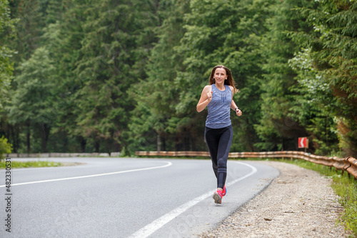 Runner woman running on the mountain road through the forest. Female sport girl training outdoors for marathon © skumer