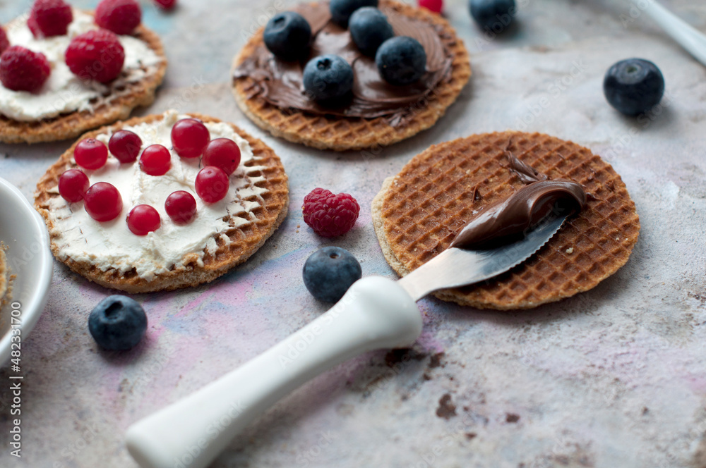 Waffles with cream cheese and chocolate, cranberries, raspberries and blueberries on a gray background. Romantic breakfast with fruits on waffles and chocolate on knife