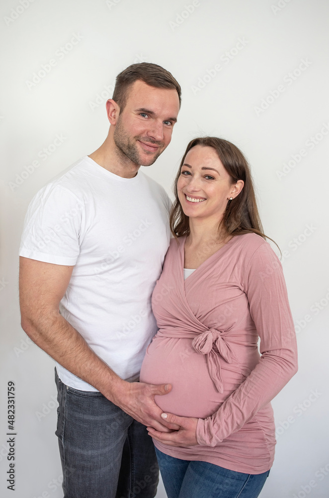 Smiling man and woman touching pregnant belly in front of white wall Smiling man and woman touching pregnant belly in front of white wall