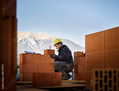 Bricklayer fixing bricks crouching at construction site