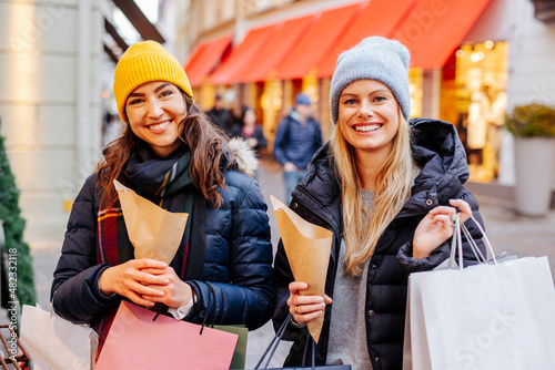 Smiling women shopping at Christmas market holding sweet chestnuts in paper bags photo