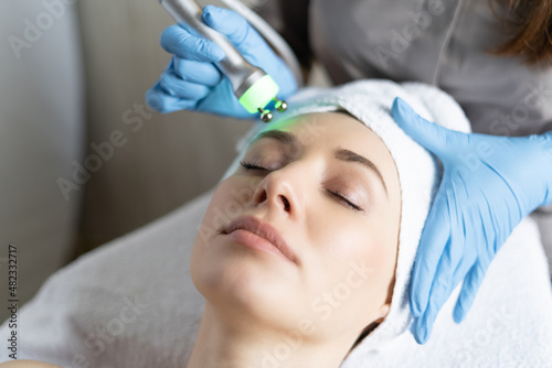 Young woman lying on cosmetologist's table during rejuvenation procedure. Cosmetologist take care about neck and face skin youthfull and wellness. Hardware face cleaning procedure
