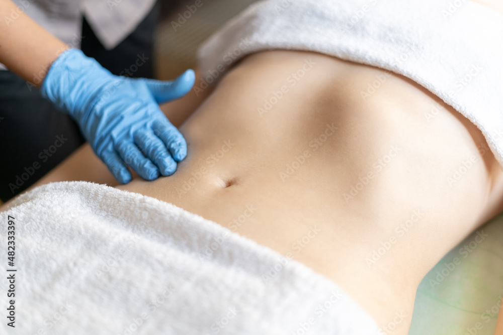 A young beautiful girl lies on the table at the beautician, hands in blue gloves do a manual massage of the abdomen