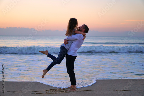 Happy Man and woman hugging on the beach in love. Lovers are happy by the sea at sunset. The husband lifted his wife in his arms. Traveling for two to the ocean. High quality photo