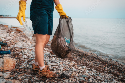 Earth day. A volunteer holds a plastic bag with garbage and poses on the beach. Close-up of feet. The concept of cleanup garbage on the ocean coast