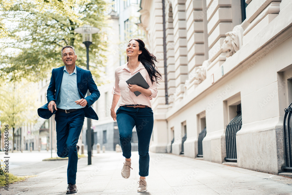 Cheerful businessman and businesswoman running on footpath in city Cheerful businessman and businesswoman running on footpath in city