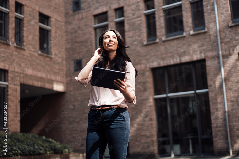 Smiling businesswoman with tablet PC standing in front of building Smiling businesswoman with tablet PC standing in front of building