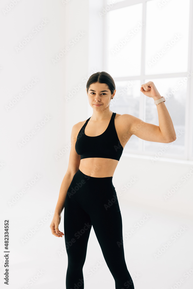 Cheerfully smiling sporty woman demonstrating biceps, isolated on white background