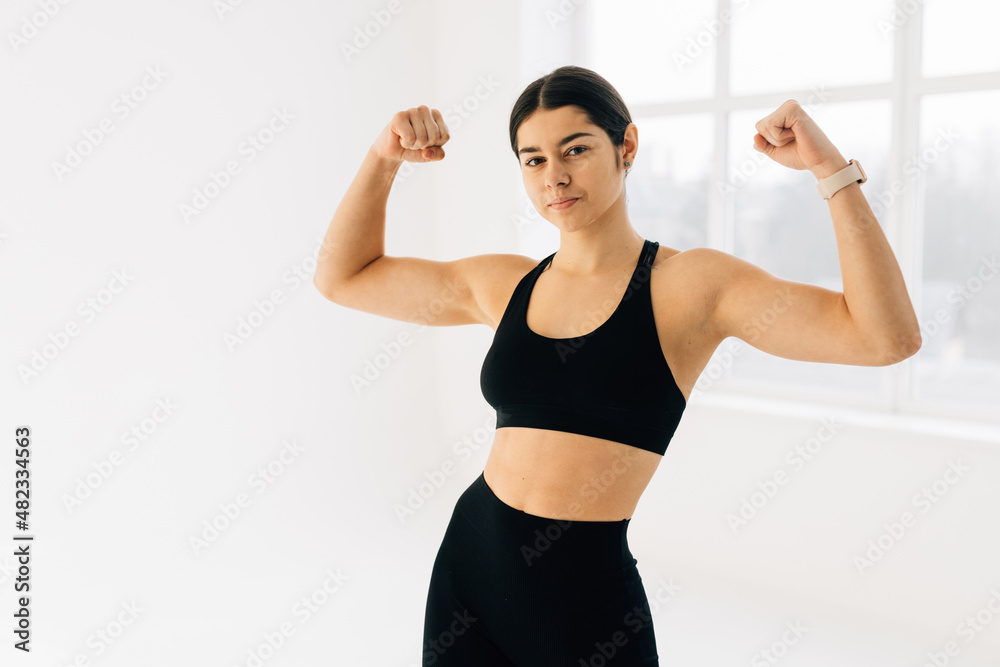 Cheerfully smiling sporty woman demonstrating biceps, isolated on white background