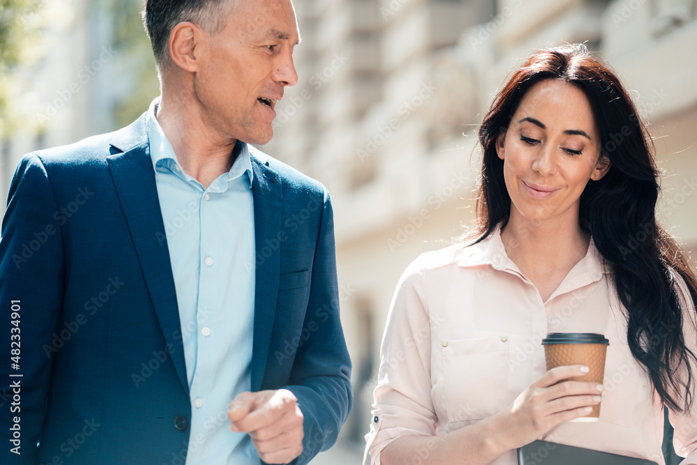 Businessman talking with businesswoman holding disposable coffee cup on sunny day Businessman talking with businesswoman holding disposable coffee cup on sunny day