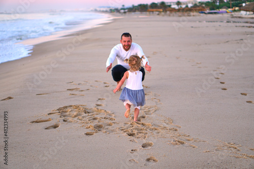 A little girl runs to her dad on the sand by the sea. The child is happy to travel with his parents. A man meets a girl beach running towards her father. open arms father on beach at the sunny day