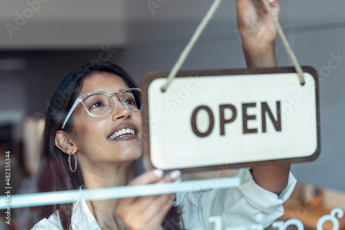 Smiling young businesswoman hanging open sign at entrance of coworking office photo