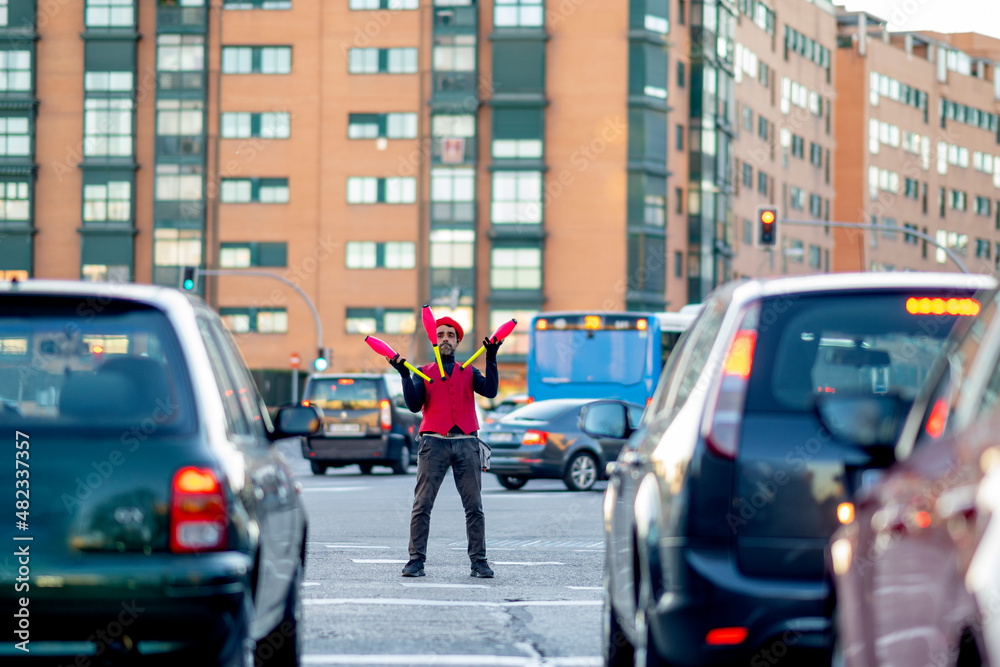 Solo performer juggling pins surrounded by cars on street in city Solo performer juggling pins surrounded by cars on street in city