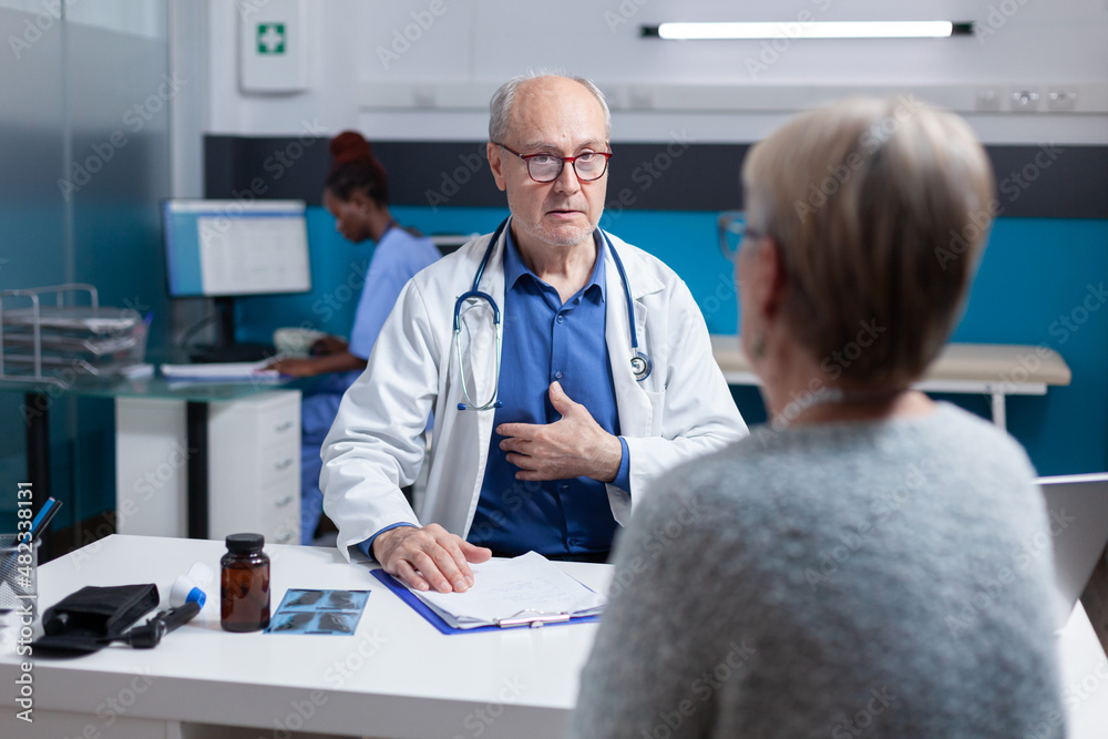 Obraz premium Medic attending consultation appointment with old woman in cabinet. Healthcare specialist and woman having conversation about disease diagnosis at annual checkup visit. Medical exam