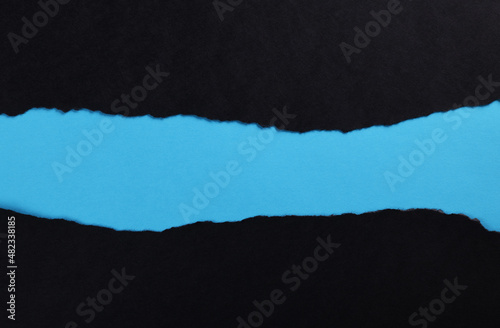 Black paper with torn edges isolated with blue colored paper background inside. Good paper texture 